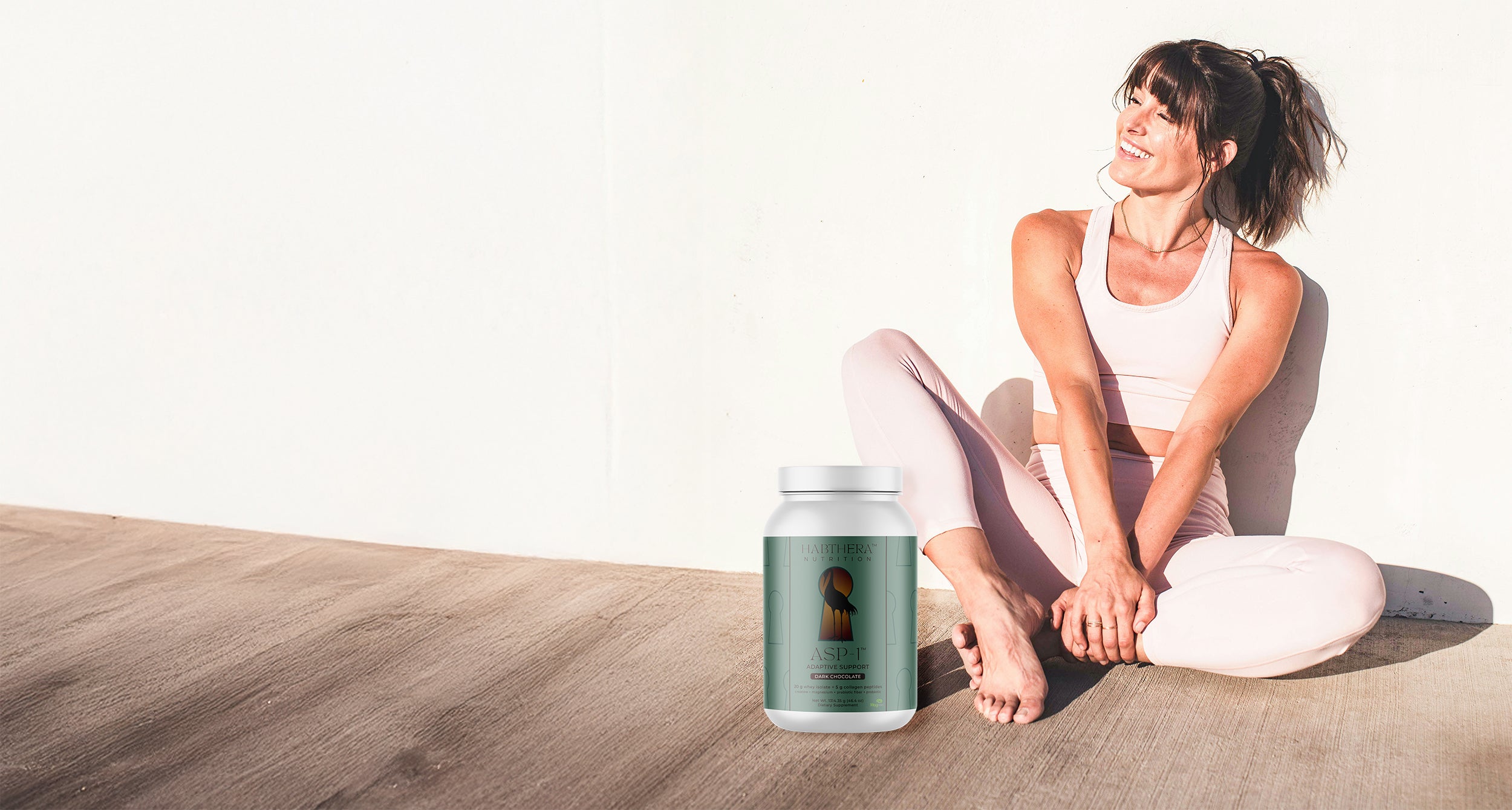 Smiling woman sitting at a table with a Habthera Nutrition supplement bottle—representing health, confidence, and balanced living.